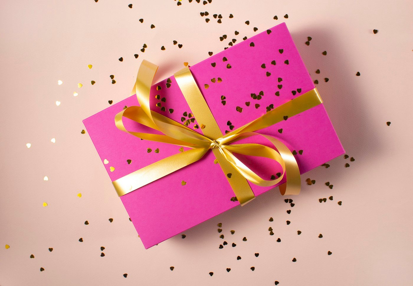 A pink gift box wrapped with a golden ribbon